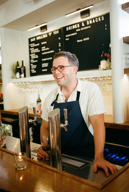man stands behind bar serving wine