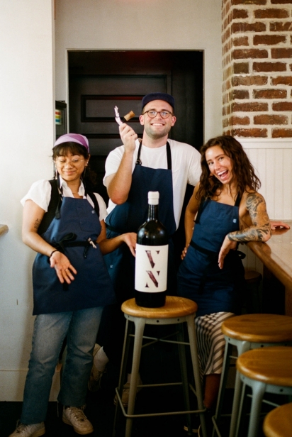 three employees pose next to large wine bottle